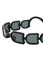 The UROKO sunglasses by ISSEY MIYAKE EYES feature a bold, chunky frame with geometric segments and dark-tinted rectangular lenses. Japanese-inspired craftsmanship creates a striking, statement accessory.