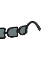 Close-up of the black temple and rim of ISSEY MIYAKE EYES UROKO sunglasses, showcasing uniquely irregular lenses and frames crafted with Japanese craftsmanship against a white background.