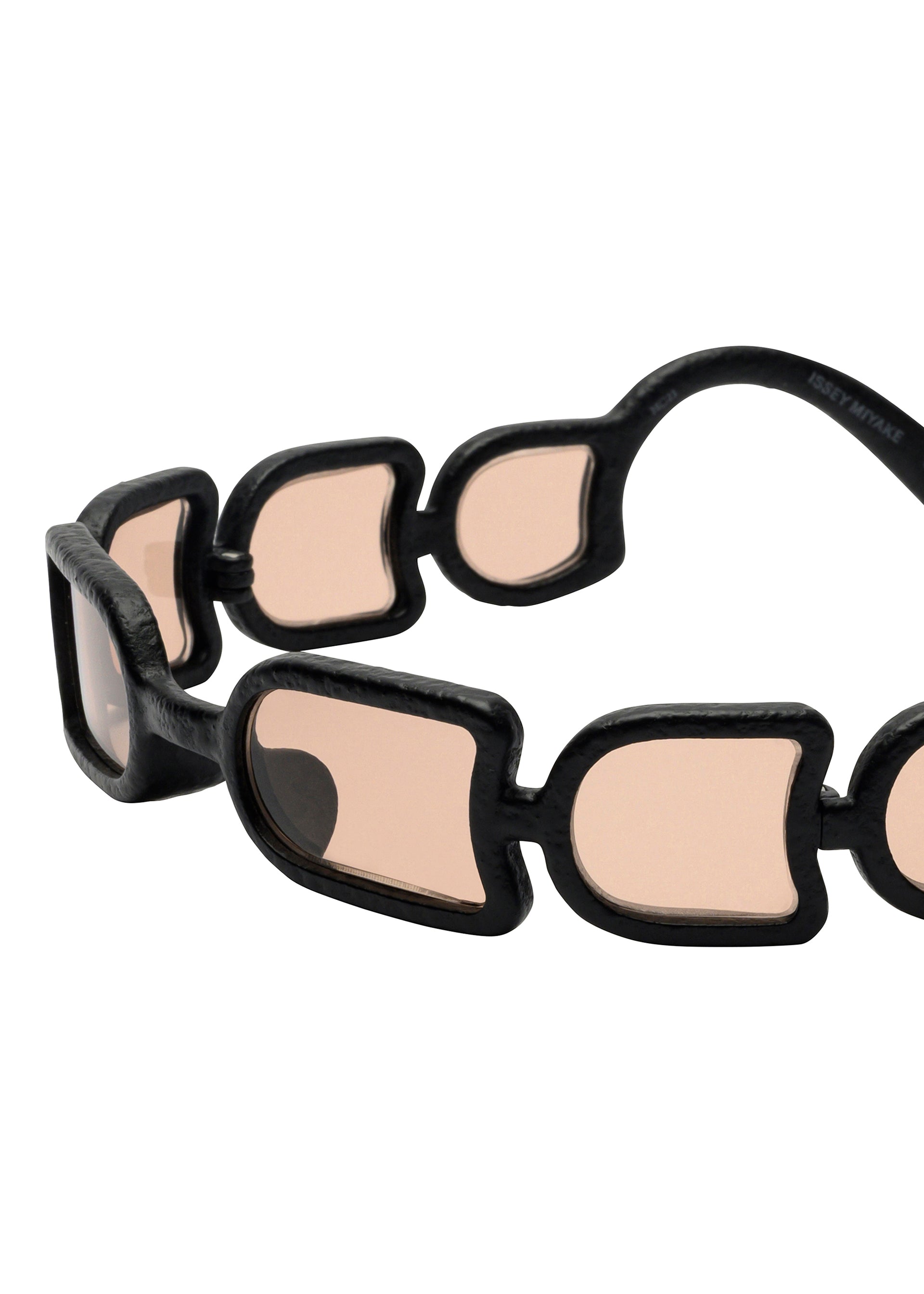 Zoomed view A close-up of ISSEY MIYAKE EYES UROKO sunglasses reveals distinctive interconnected black frames with pink-tinted lenses and a chain-like arm design, highlighting innovative Japanese craftsmanship.