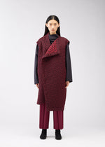 A woman with straight black hair and a neutral expression stands before a light gray backdrop, wearing the ONE CLOTH PUFF by ISSEY MIYAKE ONLINE STORE—a long burgundy jacquard vest over a dark gray top, matching pants, and black shoes.