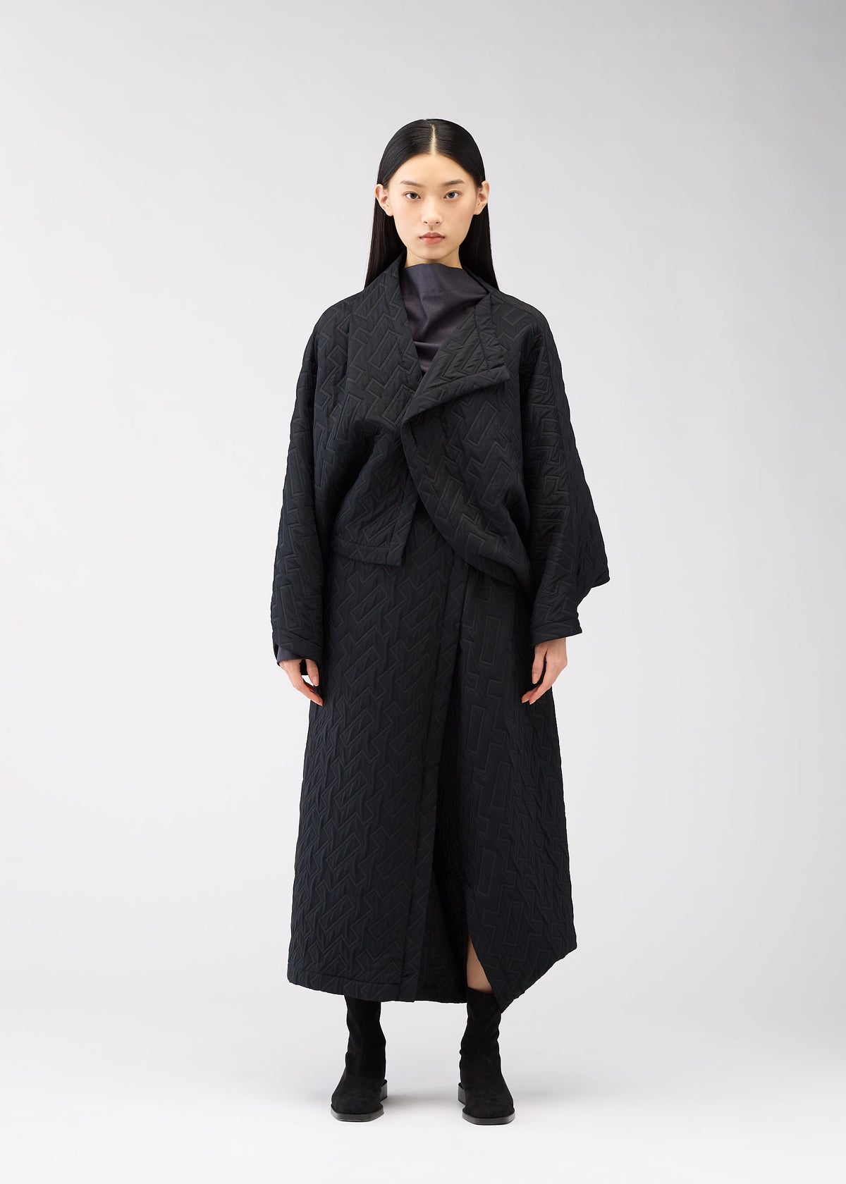 A woman with long straight black hair stands facing forward, wearing the ONE CLOTH PUFF jacket by 132 5. ISSEY MIYAKE over a dark top and black boots, against a plain white background. view 5 of 9
