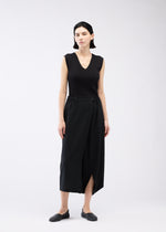 A woman with straight dark hair wears 132 5. ISSEY MIYAKE SEAMLESS BOTTOMS styled as skirt-like pants, with a sleeveless black V-neck top and black flats, standing against a plain white background.