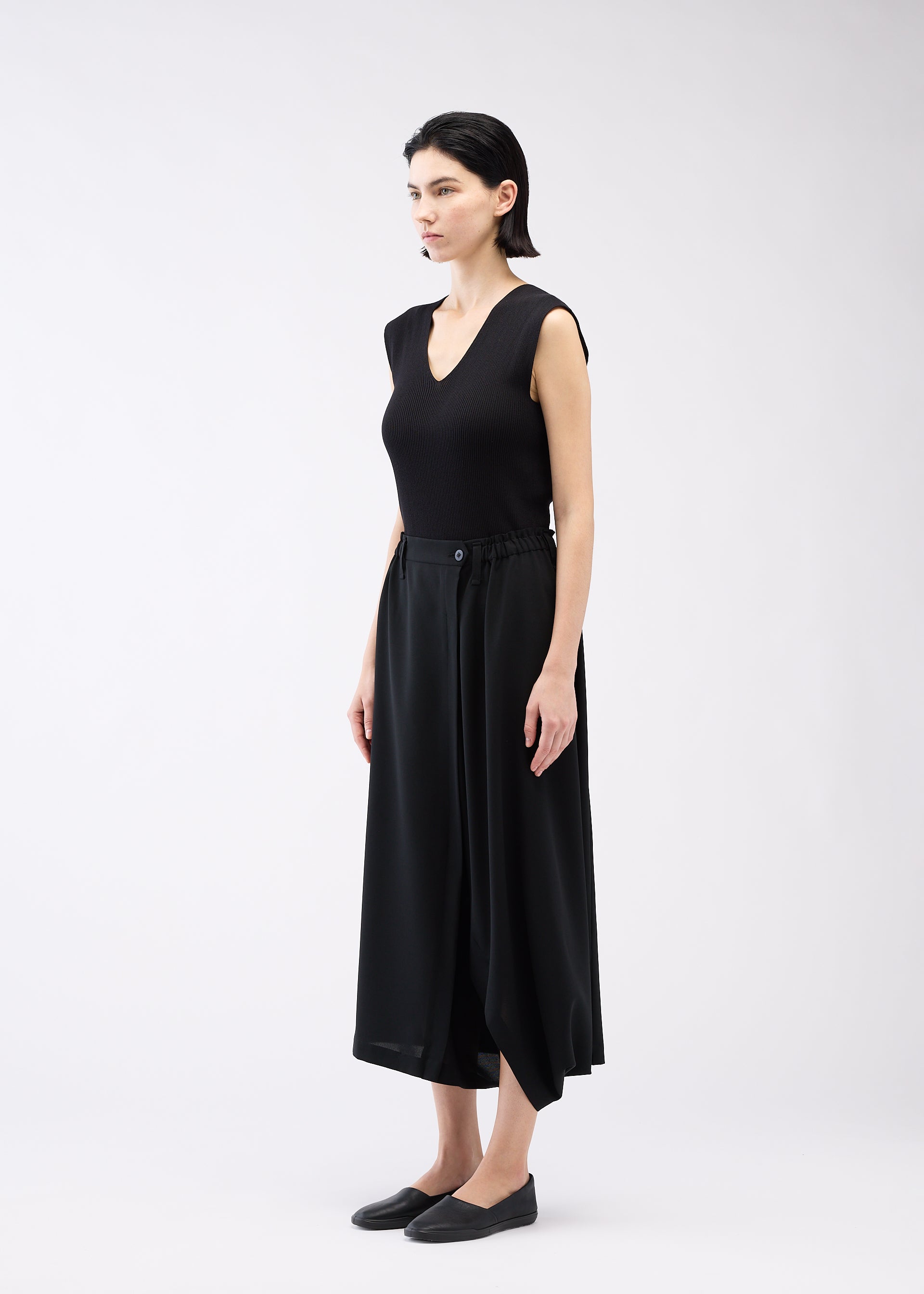 Zoomed view A woman models SEAMLESS BOTTOMS by 132 5. ISSEY MIYAKE, featuring a relaxed black sleeveless top and culotte-style pants made from recycled polyester, standing against a white background with arms at her sides.