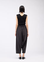 A person with short dark hair, wearing a sleeveless black top and 132 5. ISSEY MIYAKE SEAMLESS BOTTOMS with a relaxed silhouette, stands facing away from the camera against a plain white background.