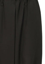 Close-up of SEAMLESS BOTTOMS by 132 5. ISSEY MIYAKE: black sarouel pants with a smooth, slightly shiny recycled polyester fabric, featuring a waistband, belt loops, and central crease.