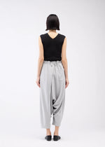 A person with short dark hair, seen from behind, wears a sleeveless black top and JERSEY BOTTOMS BASIC by 132 5. ISSEY MIYAKE—light gray, relaxed silhouette pants with an elastic waist and pocket—plus black slip-ons against a white background.