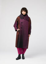 A person with curly hair wears the 132 5. ISSEY MIYAKE GRADATION COAT, long and oversized with a large collar in burgundy, brown, and black hues, styled with magenta pants and black shoes against a plain light background.