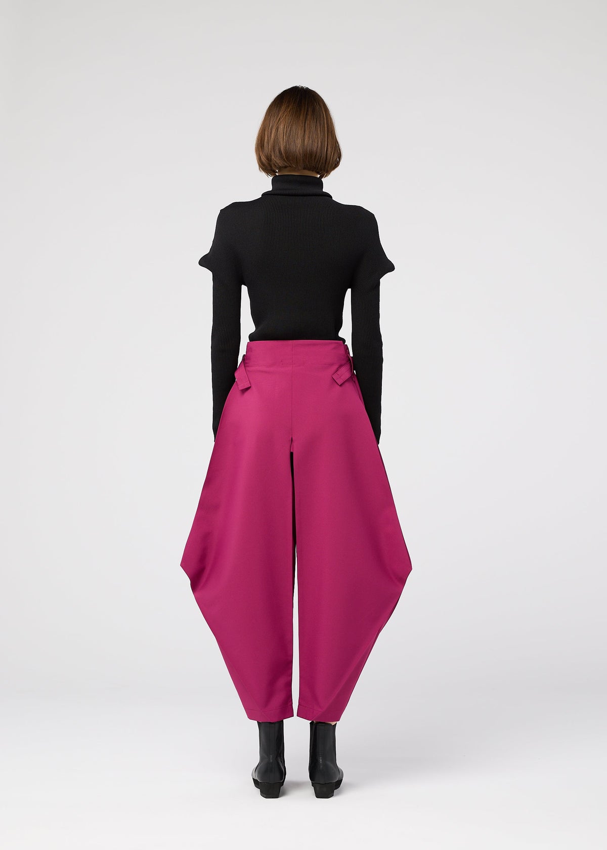 A person with short brown hair, seen from behind, wears a black turtleneck tucked into 132 5. ISSEY MIYAKE VERTEX BOTTOMS in magenta and black ankle boots, standing against a plain light background. view 10 of 12