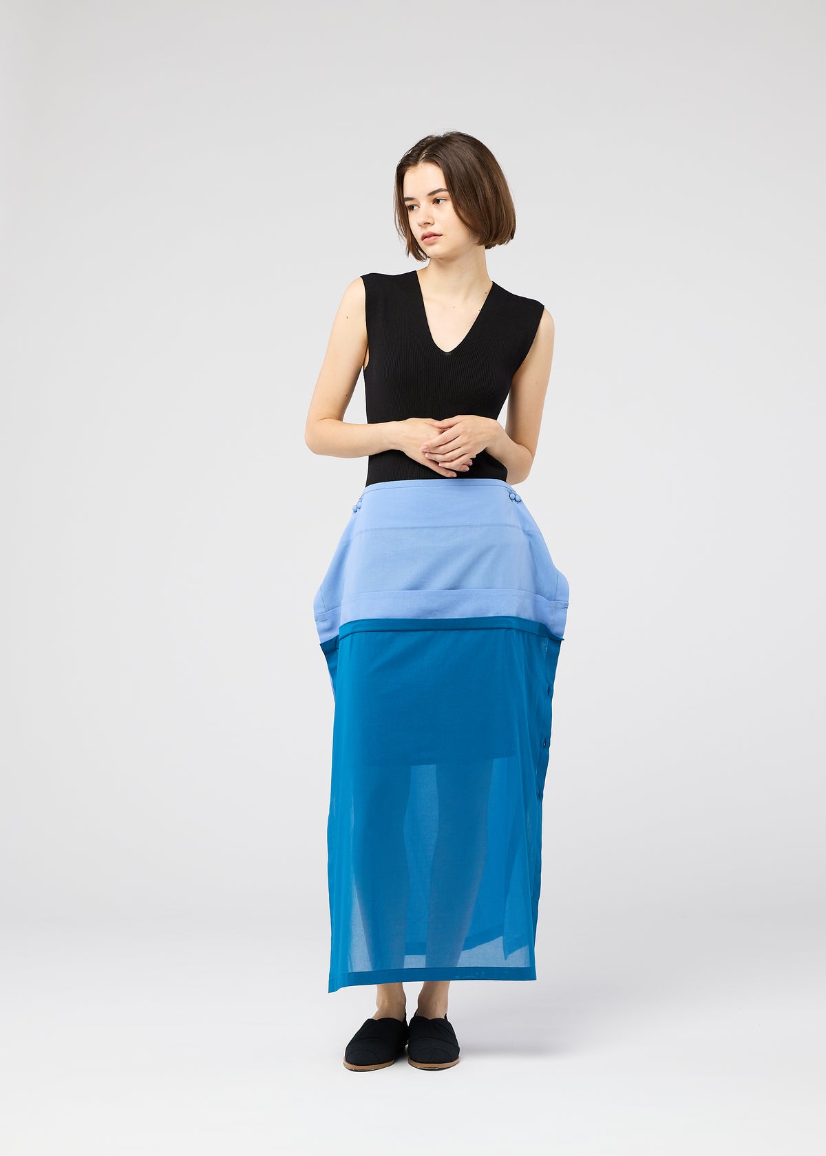 A woman with a short bob wears the SHEER FOLIO layered petticoat skirt by 132 5. ISSEY MIYAKE, paired with a sleeveless black top and black shoes, standing against a plain light gray background. view 10 of 11
