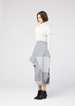A woman with short brown hair wears the NO.17 PRINT high-waisted geometric fold skirt in light gray by 132 5. ISSEY MIYAKE, paired with a white turtleneck and black ankle boots, standing against a plain light gray background.