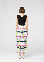 A woman with short brown hair wears the 132 5. ISSEY MIYAKE NO.6 TRANSLUCENT: a sleeveless black top and a long, colorful plaid skirt with ruffled accents and elegant folds, paired with white flats against a light background.