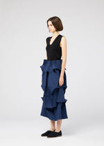 A woman in profile wears a sleeveless black top and the NO.6 SOLID skirt by 132 5. ISSEY MIYAKE, featuring bold blue geometric ruffles for a sculptural look, paired with black slip-on shoes against a plain background.