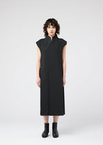 A person with short curly hair faces forward, wearing a sleeveless, ankle-length 132 5. FLAT 1 dress by 132 5. ISSEY MIYAKE and black ankle boots, against a plain light gray background.