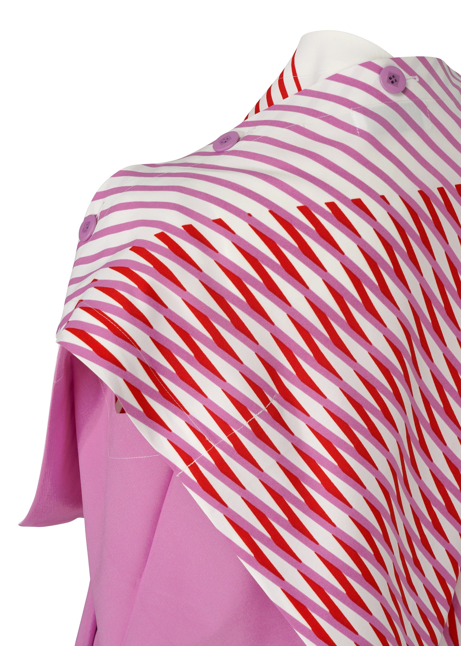 Zoomed view A person wears FACET by 132 5. ISSEY MIYAKE—a light pink garment paired with a white and red diagonally striped scarf with purple buttons draped over one shoulder. The scarf’s 3D pattern creates striking visual effects; only the torso and neck are shown.