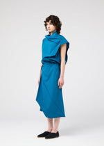 A person with curly hair stands sideways, wearing the blue FACET SOLID outfit by 132 5. ISSEY MIYAKE, made from plant-derived polyester plain fabric, and black slip-on shoes against a light gray background.
