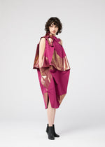 A woman with curly hair wears the 132 5. ISSEY MIYAKE NO.17 FOIL folding dress in magenta with metallic gold accents and black ankle boots, showcasing a three-dimensional silhouette against a plain light gray background.
