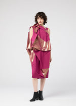 A woman with short curly hair wears the NO.17 FOIL folding dress by 132 5. ISSEY MIYAKE in magenta, featuring geometric gold foil accents and paired with black ankle boots, standing against a plain light gray background.