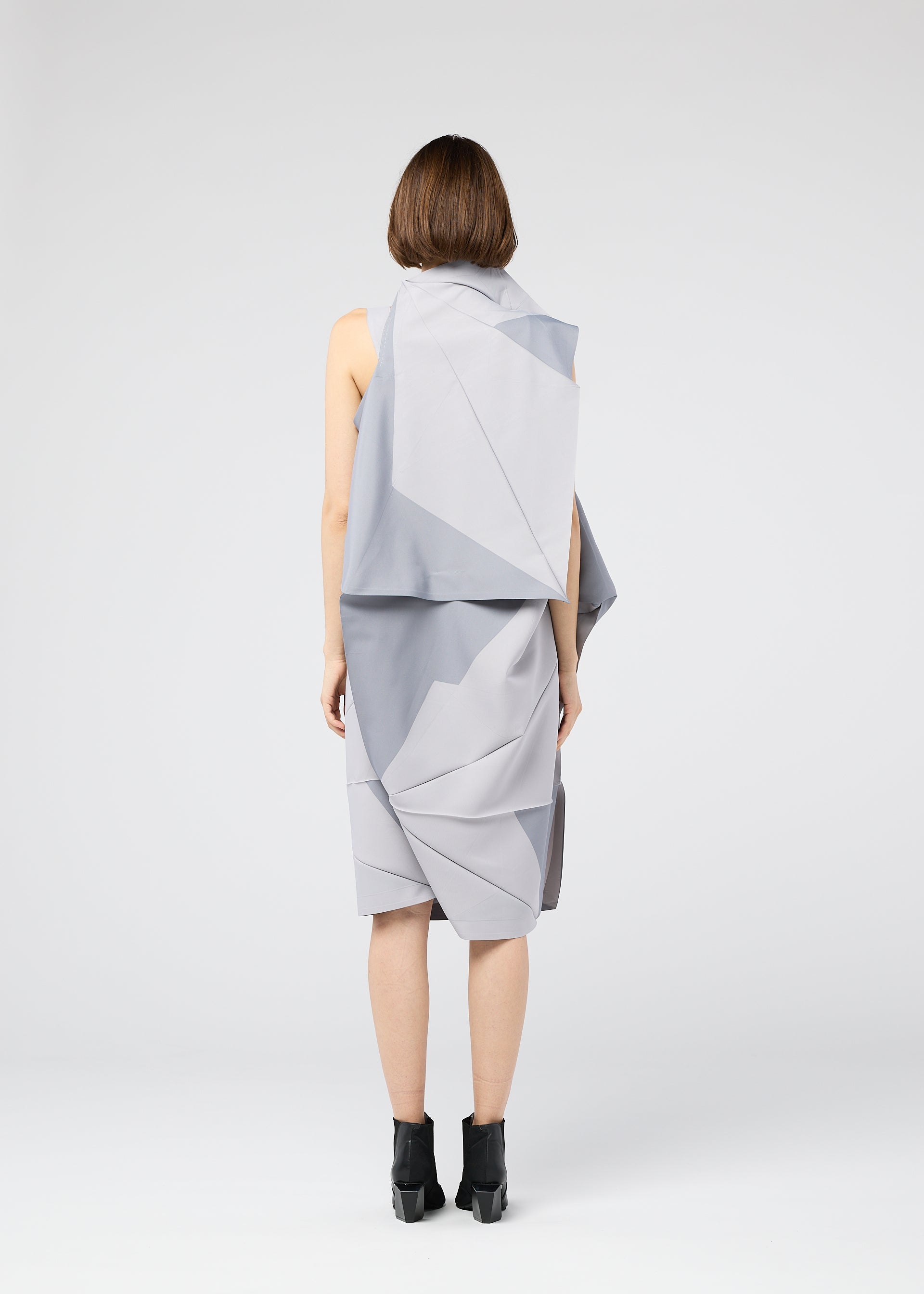 Zoomed view A person with short brown hair stands facing away, wearing the gray NO.17 PRINT dress by 132 5. ISSEY MIYAKE with angular folds and black ankle boots against a plain white background.