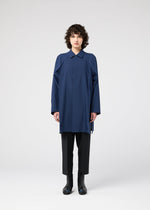 A person with short curly hair faces forward, wearing the FOLD SHIRT by 132 5. ISSEY MIYAKE—a loose blue top with raglan sleeves—paired with black pants and boots, set against a plain white background.
