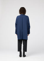 A person with curly hair stands facing away, wearing the FOLD SHIRT by 132 5. ISSEY MIYAKE—a loose-fitting, long blue shirt with raglan sleeves—over black pants and black ankle boots, against a plain white background.