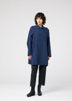 A person with curly hair wears the FOLD SHIRT by 132 5. ISSEY MIYAKE, paired with black ankle-length pants and boots, standing against a plain light gray background.