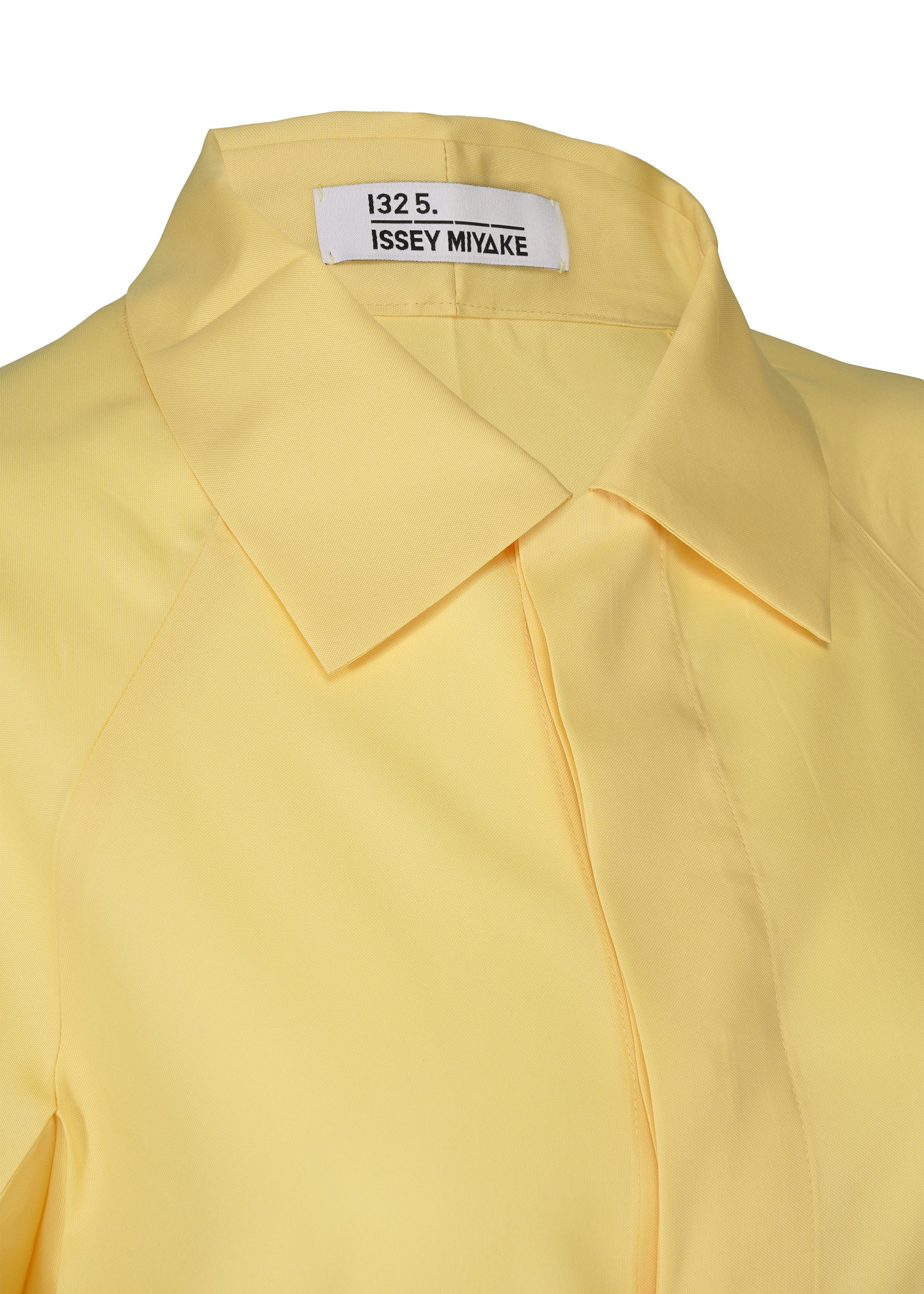 Zoomed view Close-up of a pale yellow FOLD SHIRT by 132 5. ISSEY MIYAKE, featuring a regular collar and an inner label with the brand name in black text.