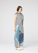A woman with short brown hair and cream flats stands in a studio wearing FACET by 132 5. ISSEY MIYAKE—a loose, sleeveless ensemble with bold black, white, blue, and red geometric stripes in a striking Nassen print for a 3D effect.