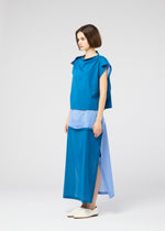 A woman with short brown hair wears the SHEER FOLIO by 132 5. ISSEY MIYAKE: a sleeveless blue top and long, layered blue skirt in various shades, paired with white slip-on shoes, standing sideways against a plain light background.
