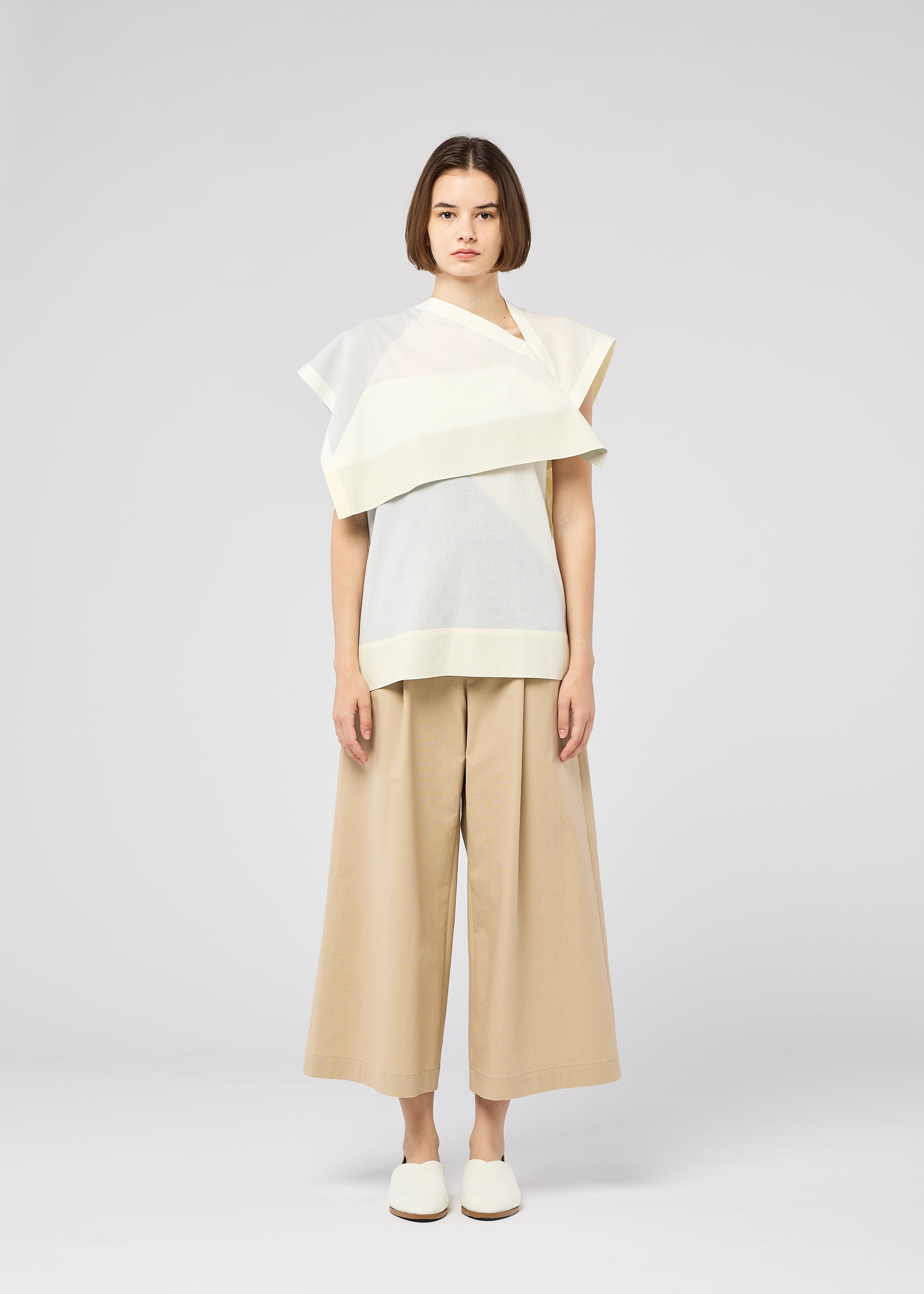 Zoomed view Against a plain light gray background, a person with straight, chin-length brown hair wears the FOLD RAMIE PRINT top by 132 5. ISSEY MIYAKE, paired with wide beige culotte pants and white slip-on shoes.