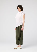 A person with short curly hair models the 132 5. ISSEY MIYAKE RADIAL FOLD SHIRT, paired with loose olive green pants and white slip-on shoes, standing against a plain background with a neutral expression.