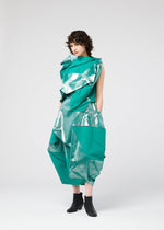 A person with curly hair models the NO.17 FOIL by 132 5. ISSEY MIYAKE, a sculptural metallic turquoise outfit with geometric folds, paired with black ankle boots, posing against a plain white background.
