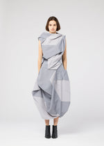 A woman stands against a plain white background wearing the NO.17 PRINT dress by 132 5. ISSEY MIYAKE with black ankle boots, arms relaxed at her sides, looking directly at the camera.