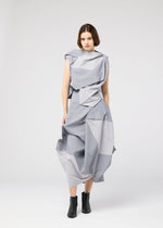 A woman stands against a plain background wearing the NO.17 PRINT dress by 132 5. ISSEY MIYAKE, featuring a sculptural light gray design with layered, angular folds, paired with black ankle boots.