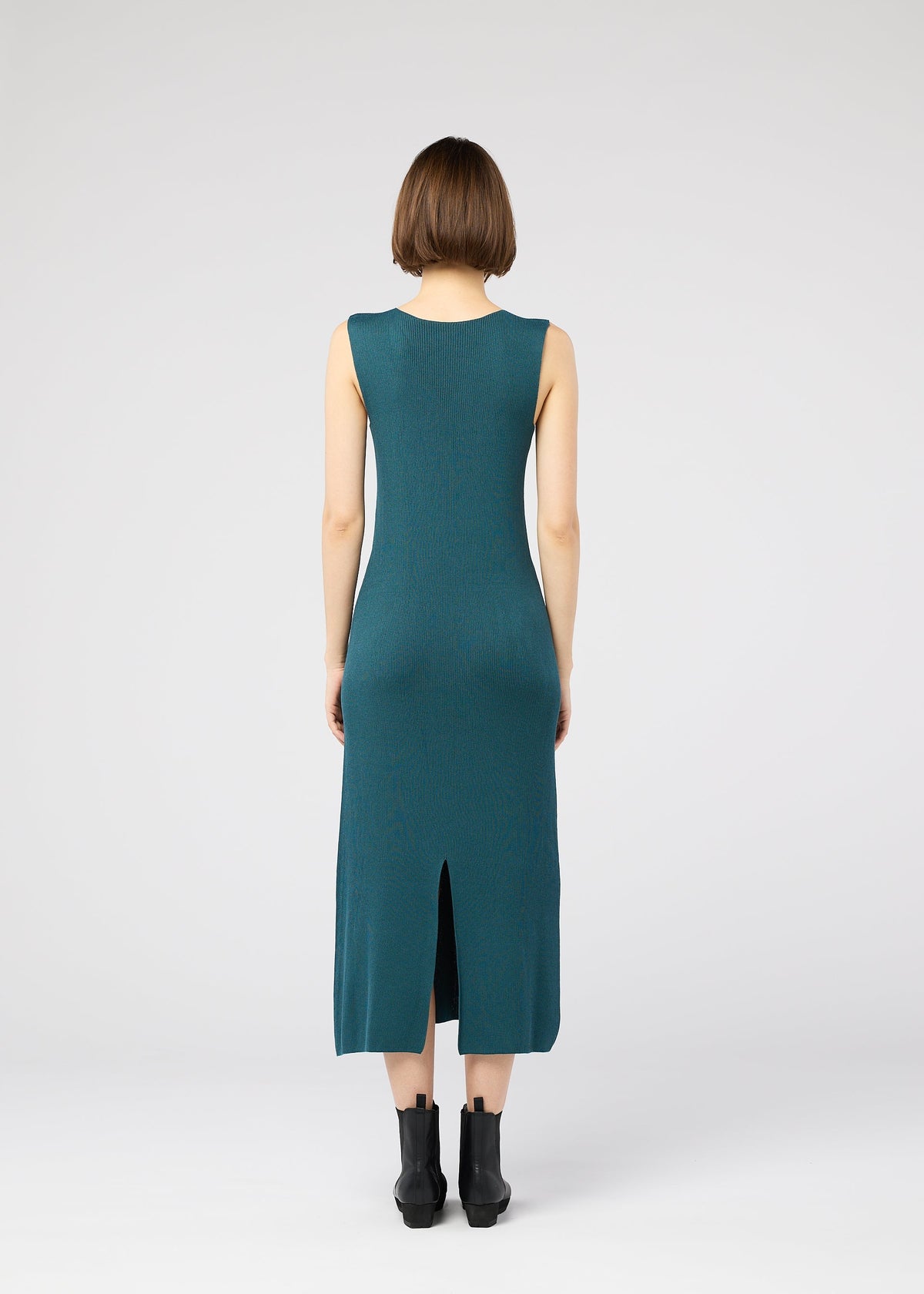 A woman with short brown hair stands with her back to the camera, wearing the teal FLAT RIB KNIT 1 dress by 132 5. ISSEY MIYAKE and black ankle boots against a plain white background. view 9 of 10