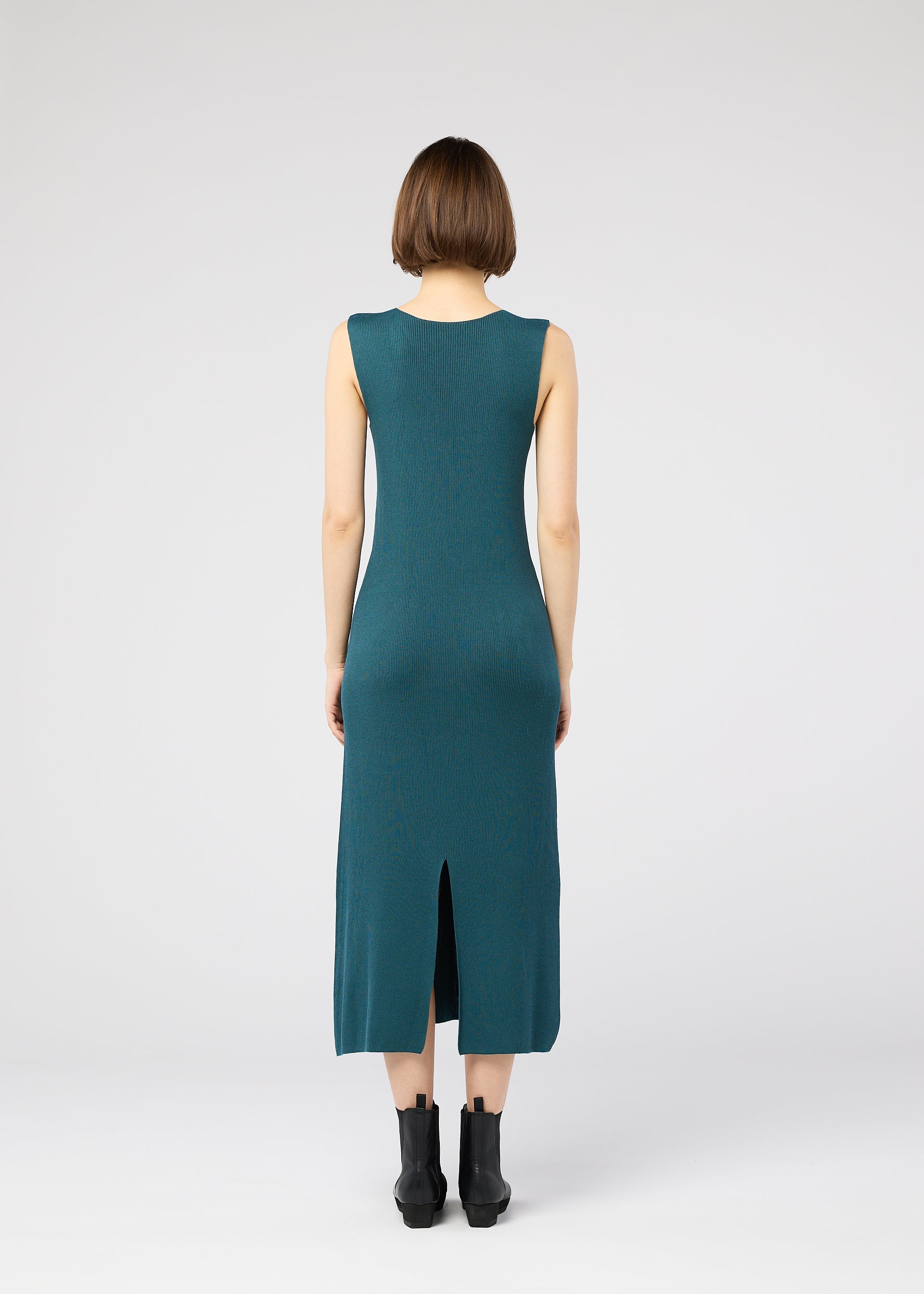 Zoomed view A woman with short brown hair stands with her back to the camera, wearing the teal FLAT RIB KNIT 1 dress by 132 5. ISSEY MIYAKE and black ankle boots against a plain white background.