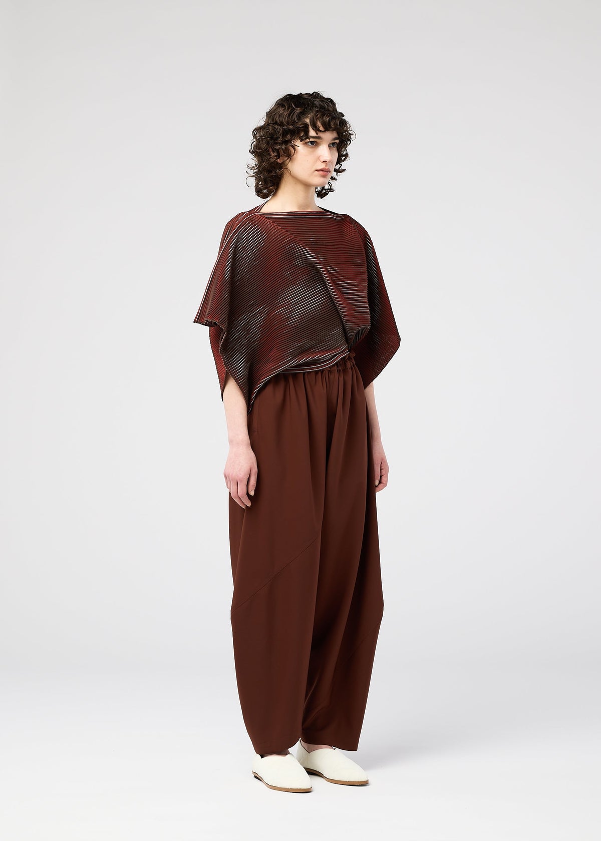 A person with curly hair stands against a plain background, wearing the FACET KNIT top and matching wide pants by 132 5. ISSEY MIYAKE, highlighting the unique knitting structure and pattern depth. view 8 of 10
