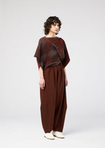 A person with curly hair stands against a plain background, wearing the FACET KNIT top and matching wide pants by 132 5. ISSEY MIYAKE, highlighting the unique knitting structure and pattern depth.
