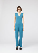 A person with straight, shoulder-length brown hair and black slip-on shoes stands facing forward against a plain white background, wearing the FLAT RIB KNIT 2 by 132 5. ISSEY MIYAKE: a seamless blue rib knit V-neck sleeveless top and matching pants.