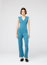 A woman with a bob stands facing forward, wearing the 132 5. ISSEY MIYAKE FLAT RIB KNIT 2 sleeveless blue V-neck top and matching moisture-wicking blue pants, paired with black slip-on shoes against a plain light background.