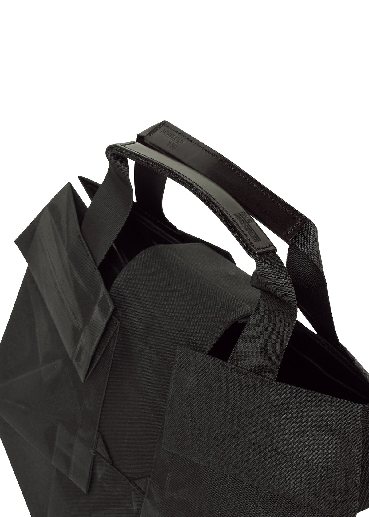 Close-up of the No.6-BG tote bag by 132 5. ISSEY MIYAKE: black fabric, sturdy reinforced handle, folding design, and a simple modern look—all against a white background for practical and stylish everyday use. view 5 of 6