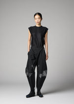 A person stands against a gray backdrop wearing the F-BT black sleeveless top and loose, angular recycled polyester pants with mesh panels by 132 5. ISSEY MIYAKE, paired with black shoes for a modern minimalist look.