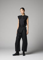 A woman models the F-BT by 132 5. ISSEY MIYAKE—sleeveless black top and belted wide-leg recycled polyester pants—against a grey background, paired with black ankle boots, arms relaxed and expression neutral.