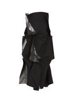 The No.1-2 dress by 132 5. ISSEY MIYAKE is a sculptural black strapless piece with a flared silhouette, showcasing angular, layered ruffles and glimpses of lustrous metallic silver foil fabric emerging from the folds.
