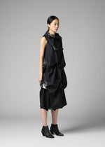 A woman with straight black hair stands in profile, wearing the 132 5. ISSEY MIYAKE No.1-1 sleeveless recycled polyester dress with sculptural layers and black ankle boots, set against a plain light gray background.