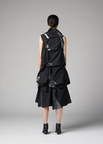 A woman with straight dark hair tied back wears the No.1-1 dress by 132 5. ISSEY MIYAKE, featuring recycled polyester, large geometric folds, and a pyramid silhouette, paired with black heels against a plain gray background.