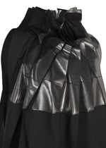 A close-up of No.3-2 by 132 5. ISSEY MIYAKE, a black recycled polyester dress featuring shiny, metallic-textured pleats and overlapping folds that create a geometric pattern across the fabric reminiscent of foil processing.