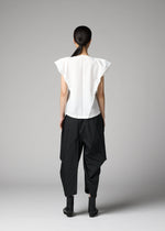 A person with long dark hair tied back stands facing away, wearing the F-SH-1 folding technique shirt by 132 5. ISSEY MIYAKE, pointed shoulders visible, paired with loose black geometric pants and black ankle boots against a gray background.