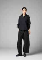 A woman with her hair tied back and a neutral expression stands before a gray backdrop, wearing the F-SH-1 folding technique shirt by 132 5. ISSEY MIYAKE, paired with wide-leg pants and matching black shoes.