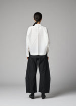 A person stands facing away, wearing the 132 5. ISSEY MIYAKE F-SH-2 shirt featuring geometric folds and wide-leg black pants. Their hair is tied back, set against a plain gray background.