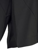Close-up of F-SH-2 by 132 5. ISSEY MIYAKE, featuring black fabric with angular, overlapping folds and a hemmed edge, reminiscent of the brand’s signature folding techniques. The lighting emphasizes the texture and sculptural structure of the material, suggesting a garment such as a skirt or pair of shorts.